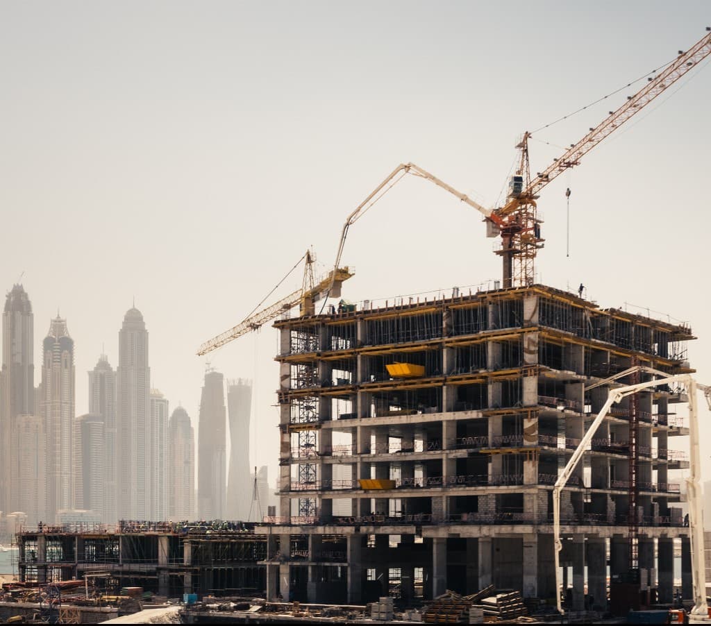 High-rise building under construction with tower cranes against a city skyline
