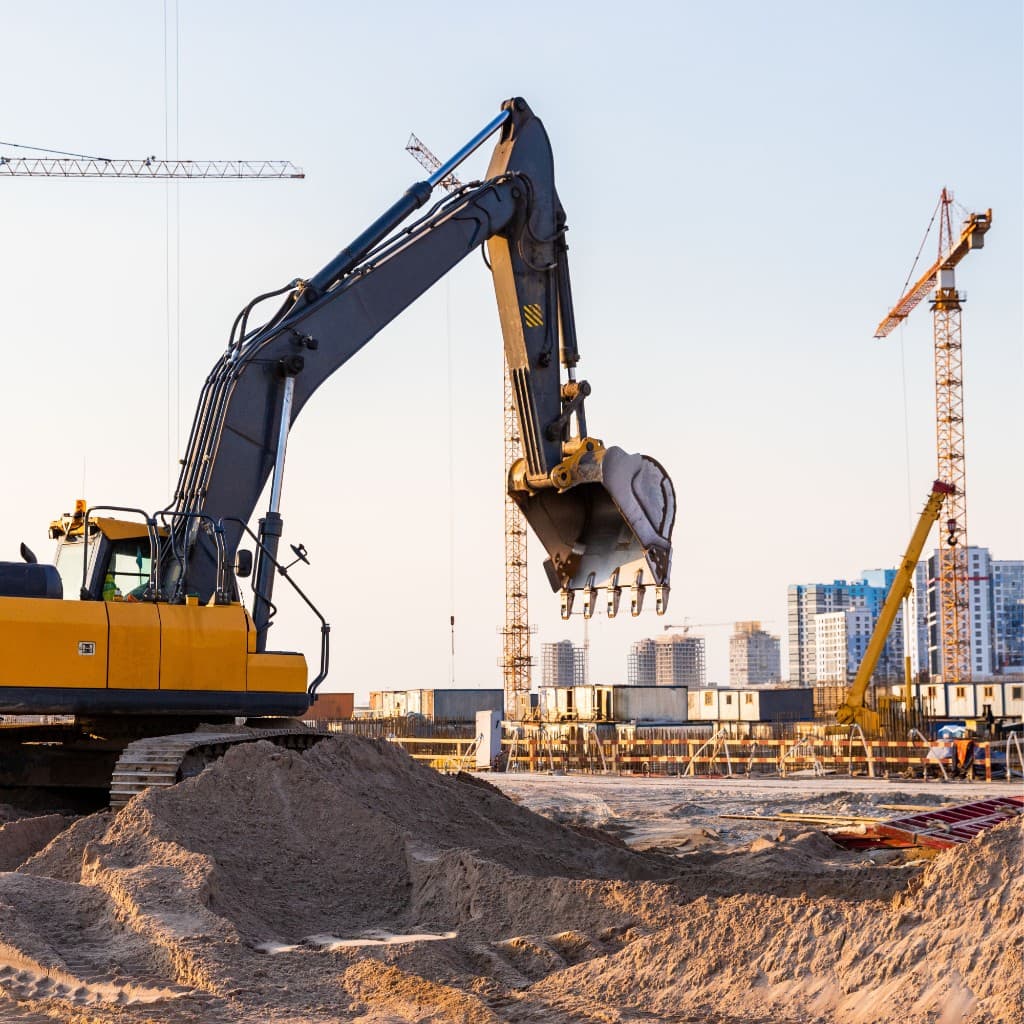 Excavator on a large urban construction site with tower cranes and high-rise buildings