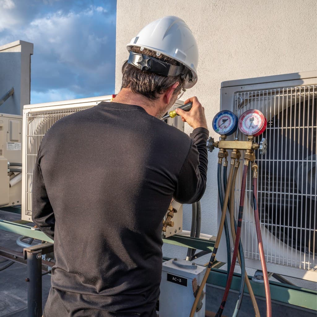 HVAC technician servicing a rooftop air conditioning unit with gauges and tools connected