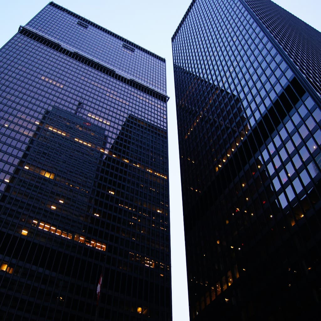 Modern glass skyscrapers viewed from below against a pale sky, representing enterprise-scale operations leaders rely on