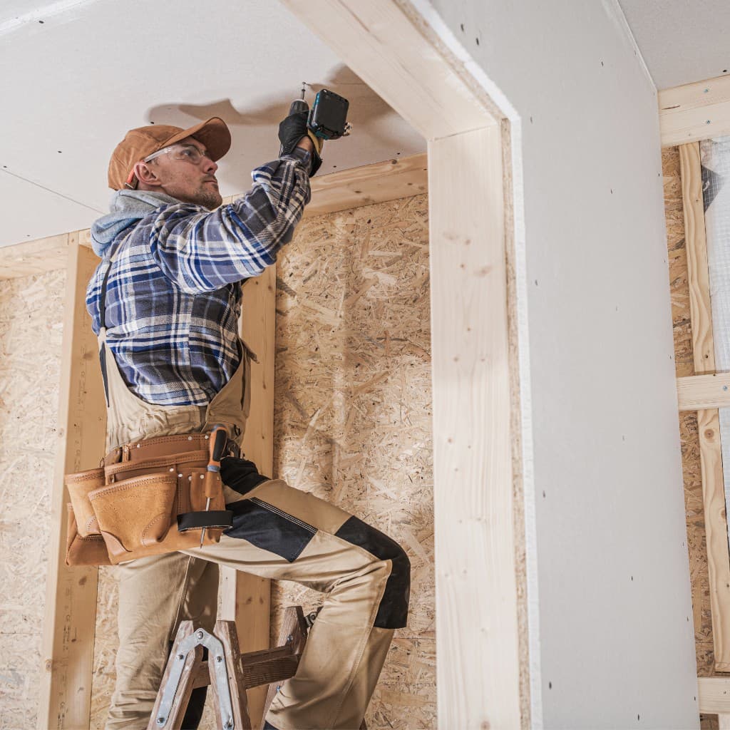 Construction worker installing ceiling drywall with a power drill